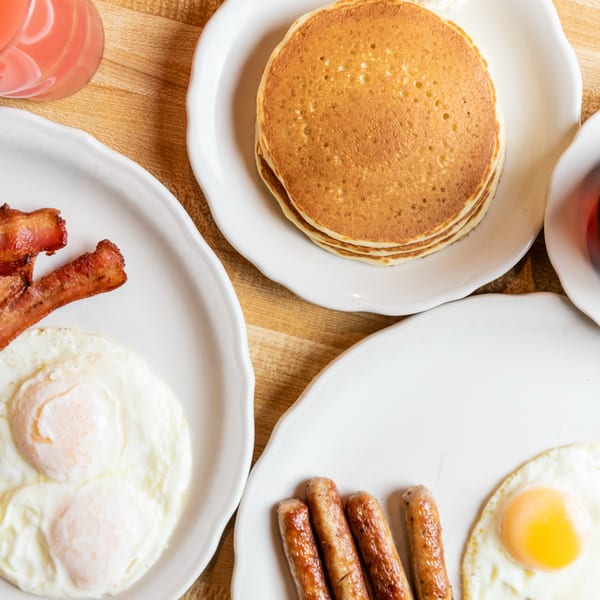 Overhead view of a breakfast spread with pancakes, bacon, eggs, sausage, and grapefruit juice.